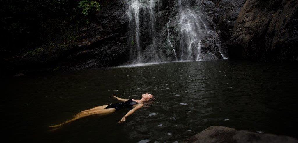 A woman swims in a cave lagoon near a waterfall.
